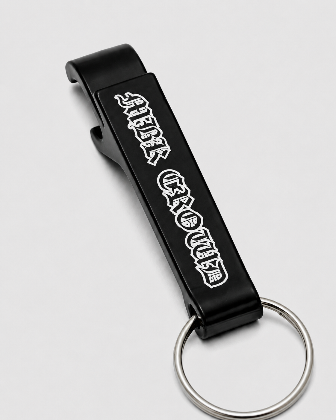 MBK Opener de perto: abridor de metal preto com MBK Crowd em letra gótica branca e argola de chaveiro